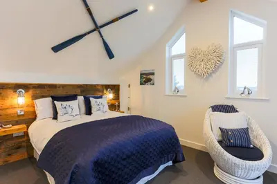 a bedroom with a bed and a chair and windows at The Lighthouse Penthouse, Studio and Holiday Home in St Ives