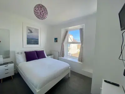a white bedroom with a bed and a window at Coast Accommodation in St Ives