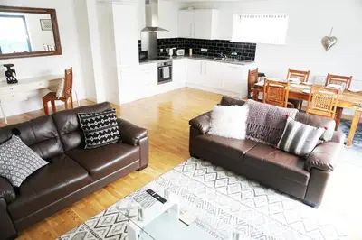 a living room with two leather couches and a kitchen at SeaQuest 8 in Newquay