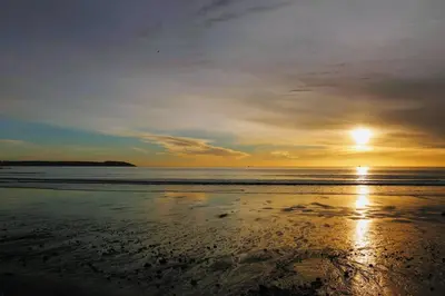 a sunset on a beach with the ocean at Porthpean Apartment in Charlestown