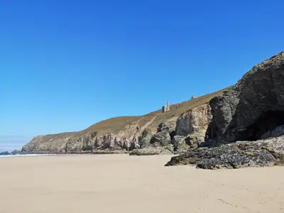 a sandy beach next to a cliff with a lighthouse at Willow - 31287 in Porthtowan