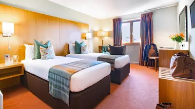 a hotel room with two beds and a chair at Lanhydrock Hotel & Golf Club in Bodmin