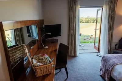 a hotel room with a desk with a mirror and a bedroom at Lanhydrock Hotel & Golf Club in Bodmin