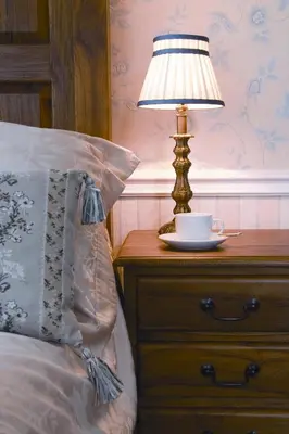 a lamp on a nightstand next to a bed with a cup on it at Rose in Vale Country House Hotel in St. Agnes