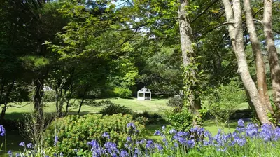 a garden with a small white house in the distance at Rose in Vale Country House Hotel in St. Agnes