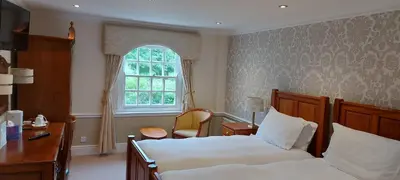 a bedroom with two beds and a desk and a window at Rose in Vale Country House Hotel in St. Agnes