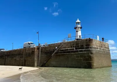 a lighthouse on a pier with a dog on the beach at Little Dolly sea view 2 bedroom apartment, St Ives town, dog friendly in St Ives
