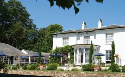 a large white house with chairs and umbrellas at Penmere Manor Hotel in Falmouth
