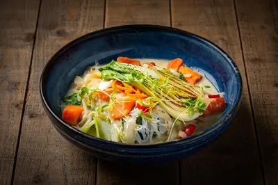 a blue bowl of soup with vegetables on a wooden table at The Norway Inn in Perranwell
