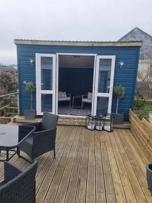 a deck with a blue house with a table and chairs at Halwyn View in St Austell