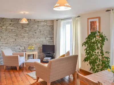 a living room with chairs and a tv and a stone wall at Little Lookover in Saint Columb Minor