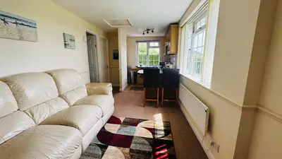 a living room with a white couch and a kitchen at Camellia Chalet in Germoe