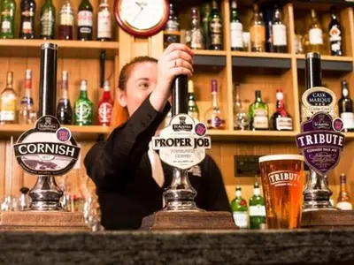 a woman behind a bar with a glass of beer at The White Hart Hotel in St Austell