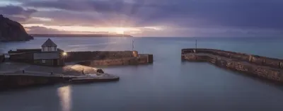 a sunset over a body of water with a lighthouse at Rashleigh Arms in St Austell