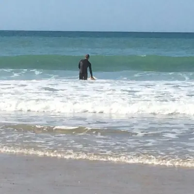 a man standing in the ocean with a surfboard at Rosevean Cottage St Agnes in St. Agnes