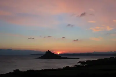 a sunset over a small island in the ocean at Wheal Rodney Holiday Park in Marazion