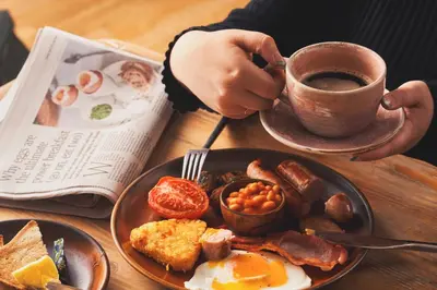 a person holding a cup of coffee next to a plate of breakfast food at Pedn-Olva in St Ives