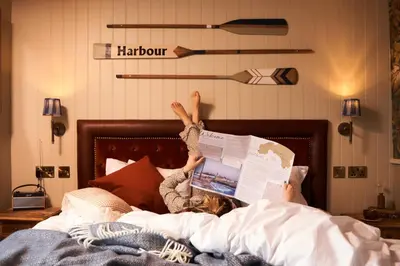 a young girl laying in bed reading a newspaper at Harbour Inn in Porthleven