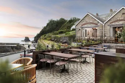 a restaurant with tables and chairs on a patio overlooking the ocean at Pier House in St Austell