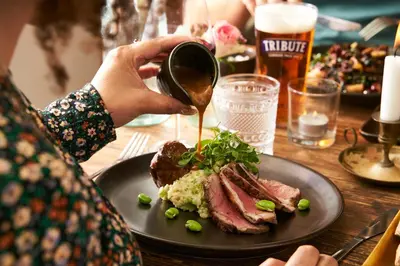 a person is pouring sauce onto a plate of food at Pier House in St Austell