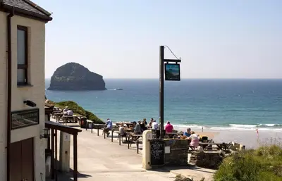 a group of people sitting at tables near the beach at Port William Inn in Tintagel