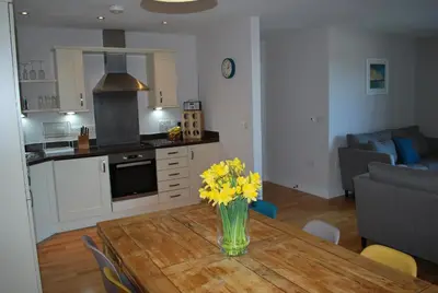 a kitchen and living room with a table with yellow flowers on it at For the Shore, Fistral Beach Newquay - 2 Bed 2 bath - Private Parking with garage for 2 vehicles in Newquay