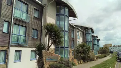 an apartment building with palm trees next to a street at For the Shore, Fistral Beach Newquay - 2 Bed 2 bath - Private Parking with garage for 2 vehicles in Newquay