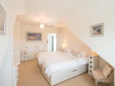 a white bedroom with a bed and a chair at Spiral View in Perranporth