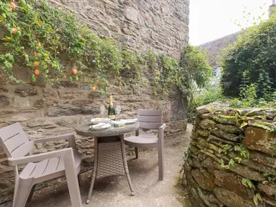 a table and chairs in a garden with a stone wall at Mithian Cottage in St. Agnes
