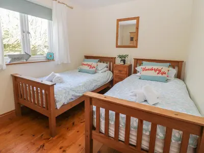 a bedroom with two beds and a mirror at Honeysuckle Cottage in Helston