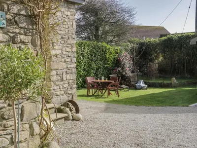 a stone building with a table and chairs in a garden at Honeysuckle Cottage in Helston