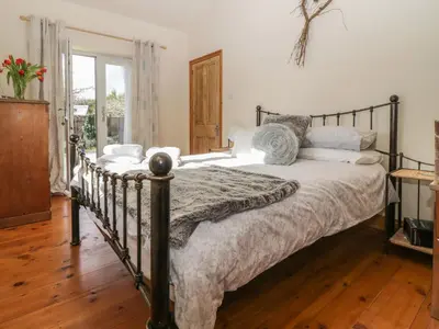 a bedroom with a large bed with a wooden floor at Honeysuckle Cottage in Helston