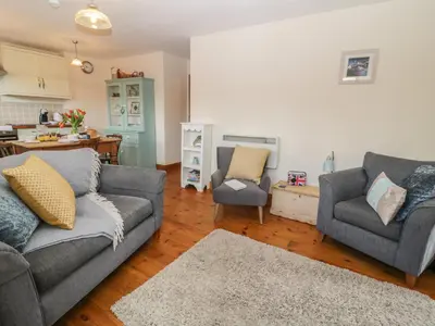 a living room with two couches and a kitchen at Honeysuckle Cottage in Helston