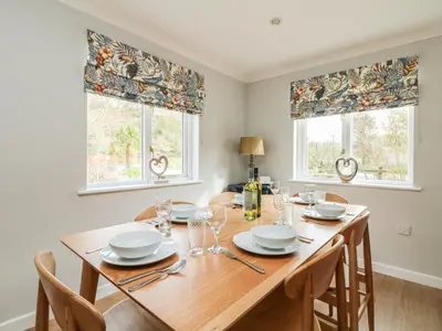 a dining room with a wooden table and two windows at Heather's Cottage in Budock Water