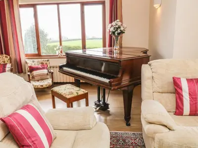 a piano in a living room with two chairs at Higher Kernick Farm in Launceston