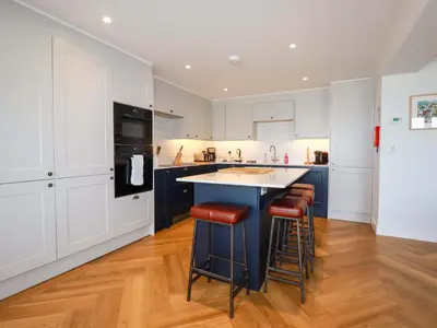 a kitchen with white cabinets and a blue island with stools at Pink House in Mevagissey