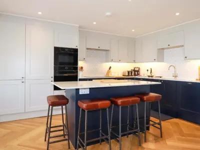 a kitchen with white cabinets and a blue island with stools at Pink House in Mevagissey
