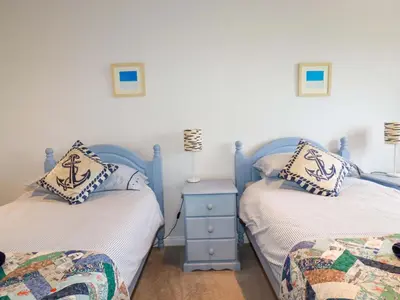 a bedroom with two beds and a table with a lamp at Pink House in Mevagissey