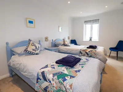 a bedroom with two beds and a blue chair at Pink House in Mevagissey