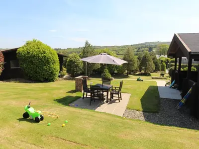 a garden with a table with an umbrella and a toy at Hazel Lodge in Bodmin