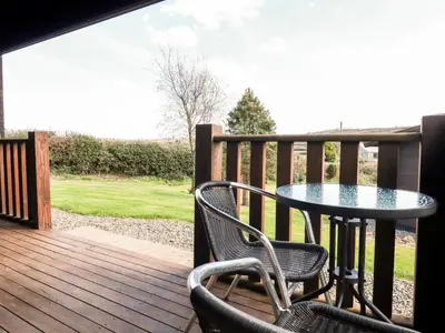 a patio with a table and chairs on a deck at Cherry Lodge in Bodmin