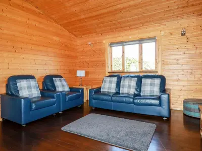 two blue leather couches in a room with wooden walls at Maple Lodge in Bodmin
