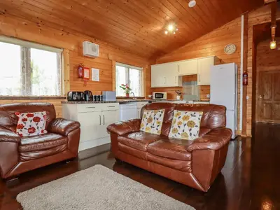 a living room with two leather chairs and a kitchen at Cedar Lodge in Bodmin