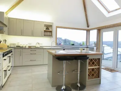 a kitchen with white cabinets and a large window at Treetops in Fowey