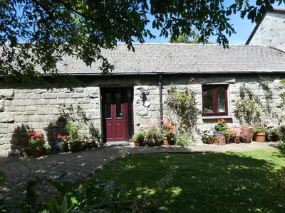 a stone cottage with a red door and some plants at Brunnion Cottage in Hayle