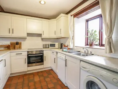 a kitchen with white cabinets and a sink and a window at Brunnion Cottage in Hayle