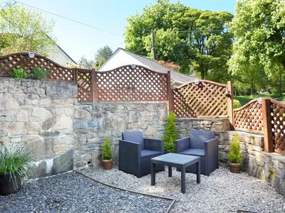 a patio with two chairs and a table next to a stone wall at Hele Stone Cottage in Launceston