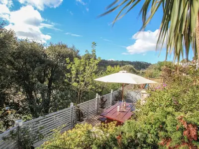 a wooden table with an umbrella in a garden at Sea Cliff Cottage in Pentewan