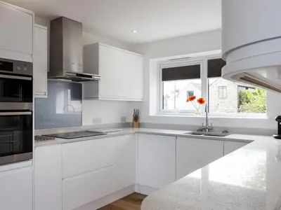 a white kitchen with white cabinets and a window at Godrevy in St Ives