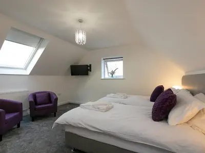 a bedroom with a large bed with two purple chairs at Godrevy in St Ives